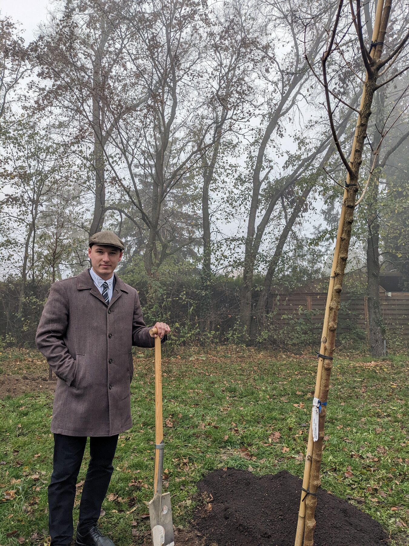 Alfonso Menanno holding a shovel beside a newly planted tree